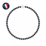 Le Collier NOELYSE de Perlinea, orné de perles noires de 7/8 mm et d'un fermoir en or blanc, est présenté dans un cercle sur fond blanc. Un écusson rond bleu avec le drapeau français et la mention "Artisan Bijoutier Français" apparaît en haut à gauche.