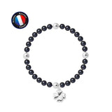 Le bracelet Perlinea Porte Bonheur Trêfle - Perles d'Eau Douce Black Tahiti présente une alternance de perles noires et argentées avec une breloque trèfle argentée, et affiche un logo rond bleu, blanc et rouge "Artisan Bijoutier Français" dans le coin supérieur gauche.