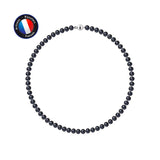 Le Collier NOELYSE de Perlinea, composé de Perles Noires de 6/7 mm et d'une Boule Fermoir d'Argent 925, est présenté dans un cercle sur fond blanc. Un insigne du drapeau français en haut à gauche indique "Artisan Bijoutier Français".