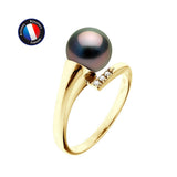 La Bague AMARA | Or Jaune de Perlinea présente une perle de Tahiti ronde et foncée et trois petits diamants sertis en or jaune, sur fond blanc, avec l'étiquette circulaire de l'artisan Perlinea dans le coin supérieur gauche.