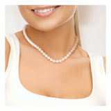 Une femme vêtue d'un haut blanc sans manches porte le Perlinea Collier NOELYSE-Or Jaune & Perles Blanches (7/8 mm). Seuls son sourire, le bas de son visage et le haut de son torse sont visibles.