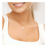 Une femme sourit doucement, portant un haut blanc et le Perlinea Collier Or Blanc Perles de Culture Rose 9-10 mm. L'image est recadrée pour ne laisser apparaître que la bouche, le cou et le haut de la poitrine.