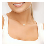 Une femme sourit, vêtue d'un haut blanc et portant le collier Perlinea Collier SOFIA | Perle Blanche, un collier délicat composé d'une seule perle ronde. L'image est recadrée de près pour mettre en évidence le bas de son visage et son cou.