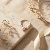 Bague en argent 925 sertie d'une perle de culture rose, posée sur marbre.