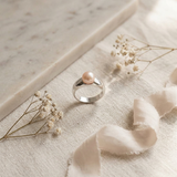 Bague en argent 925 sertie d'une perle de culture rose, posée sur tissu beige.
