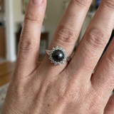Bague en argent 925 ornée d'une perle noire entourée de diamants, portée à la main.