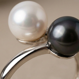 Gros plan sur deux perles, blanche et noire de Tahiti, serties en or blanc sur bague duo.