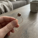 Bague en or blanc 9 carats sertie d'une perle de culture chocolat, tenue entre les doigts.