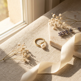Bague ouverte en or jaune 9 carats ornée d'une perle de culture blanche, posée sur un tissu beige.