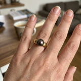 Bague en or jaune 9 carats sertie d'une perle de Tahiti noire portée à l'annulaire.