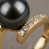 Gros plan sur le sertissage de diamants et la perle noire de Tahiti d'une bague en or jaune.