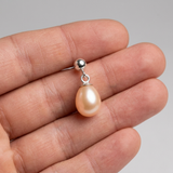 Boucle d'oreille or blanc 9 carats avec perle de culture rose suspendue, tenue dans une main.
