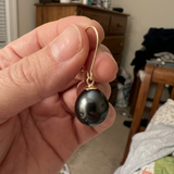 Boucle d'oreille or jaune 9 carats avec perle de culture poire noire de Tahiti, tenue en main.