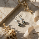 Boucles d'oreilles argent 925 en forme de cœur avec perles noires pendantes sur tissu beige.