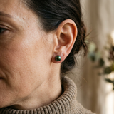 Boucles d'oreilles bouton en or jaune avec perle de culture verte, portées à l'oreille.