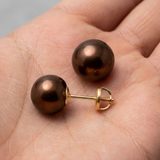 Boucles d'oreilles bouton en or jaune et perles de culture chocolat, tenues dans une paume.