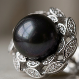 Gros plan sur la perle noire de Tahiti d'une boucle d'oreille en argent 925 à monture feuillage.