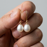 Boucles d'oreilles en or jaune 9 carats avec perles de culture poire blanches tenues en main.