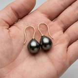 Boucles d'oreilles en or jaune avec perles de Tahiti grises présentées dans une paume.