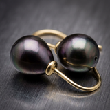 Boucles d'oreilles or jaune 9 carats avec deux perles de Tahiti noires irisées, posées sur fond gris.