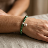 Bracelet en perles d'eau douce vertes rondes avec charm cœur en argent 925, porté au poignet.