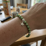 Bracelet en perles d'eau douce vertes rondes et argent 925 avec charm étoile, porté au poignet.