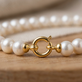 Gros plan sur le fermoir anneau en or jaune 9 carats du bracelet de perles blanches.