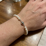 Bracelet perles blanches 5/6 mm argent 925 avec fermoir boule, porté au poignet.