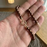 Bracelet en perles chocolat et or jaune 9 carats tenu dans une main ouverte.