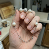 Bracelet en argent 925 avec perles de culture blanches et bille pavée, tenu dans une main.