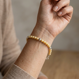 Bracelet perles d'eau douce dorées et argent 925 porté au poignet, avec fermoir réglable.