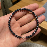 Bracelet perles noires 5/6 mm argent 925 avec fermoir boule, présenté dans une main ouverte.