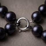 Gros plan sur le fermoir boule argenté d'un bracelet en perles noires.
