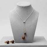 Collier lasso et boucles d'oreilles à perles chocolat sur présentoir gris.