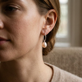 Boucles d'oreilles créoles argent 925 avec perle de culture rose portées à l'oreille.