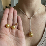 Collier lariat et boucles d'oreilles puces ornés de perles dorées, portés et tenus en main.