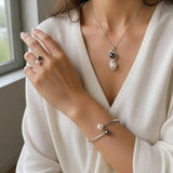 Parure bague, bracelet et collier ornés de perles blanches et noires, portée sur main, poignet et cou.