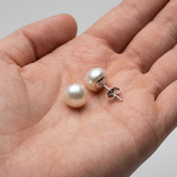 Puces d'oreilles en or blanc 9 carats avec perles blanches, présentées dans une paume de main.
