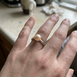 Bague jonc en argent 925 ornée d'une perle de culture rose, portée à la main.