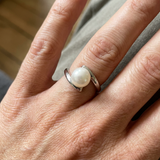 Bague en or blanc 9 carats sertie d'une perle de culture blanche, portée à l'index.