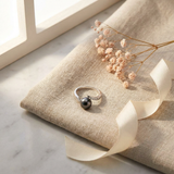 Bague en or blanc 9 carats sertie d'une perle noire de Tahiti, posée sur un coussin en lin.