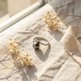 Bague or blanc 9 carats et perle de Tahiti grise posée sur lin beige.