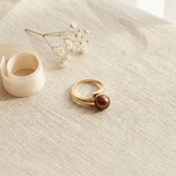 Bague or jaune 9 carats ornée d'une perle de culture chocolat, posée sur tissu beige.