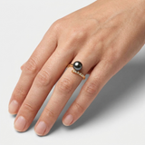 Bague or jaune 9 carats et perle de culture noire de Tahiti portée à la main.