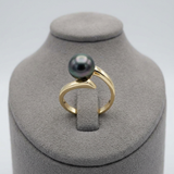 Bague or jaune 9 carats ornée d'une perle de Tahiti noire aux reflets verts, posée sur présentoir.