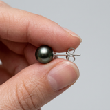 Boucle d'oreille clou argent 925 avec perle de Tahiti noire verte, tenue entre les doigts.