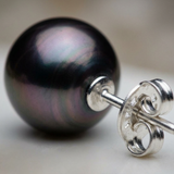 Gros plan d'une boucle d'oreille bouton en or blanc avec perle de Tahiti noire irisée et sa poussette.