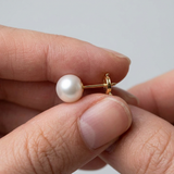 Boucle d'oreille bouton or jaune 9 carats avec perle de culture blanche tenue entre les doigts.
