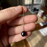 Boucle d'oreille pendante en or blanc avec chaîne fine et perle de culture noire de Tahiti.