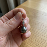 Boucles d'oreilles argent 925 étoile et perle noire en main.